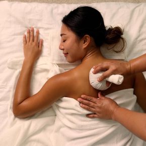 Top view of Young Asian woman receiving back massage with Thai herbal compress ball at spa salon by professional masseuse, Spa treatment and thai massage concept